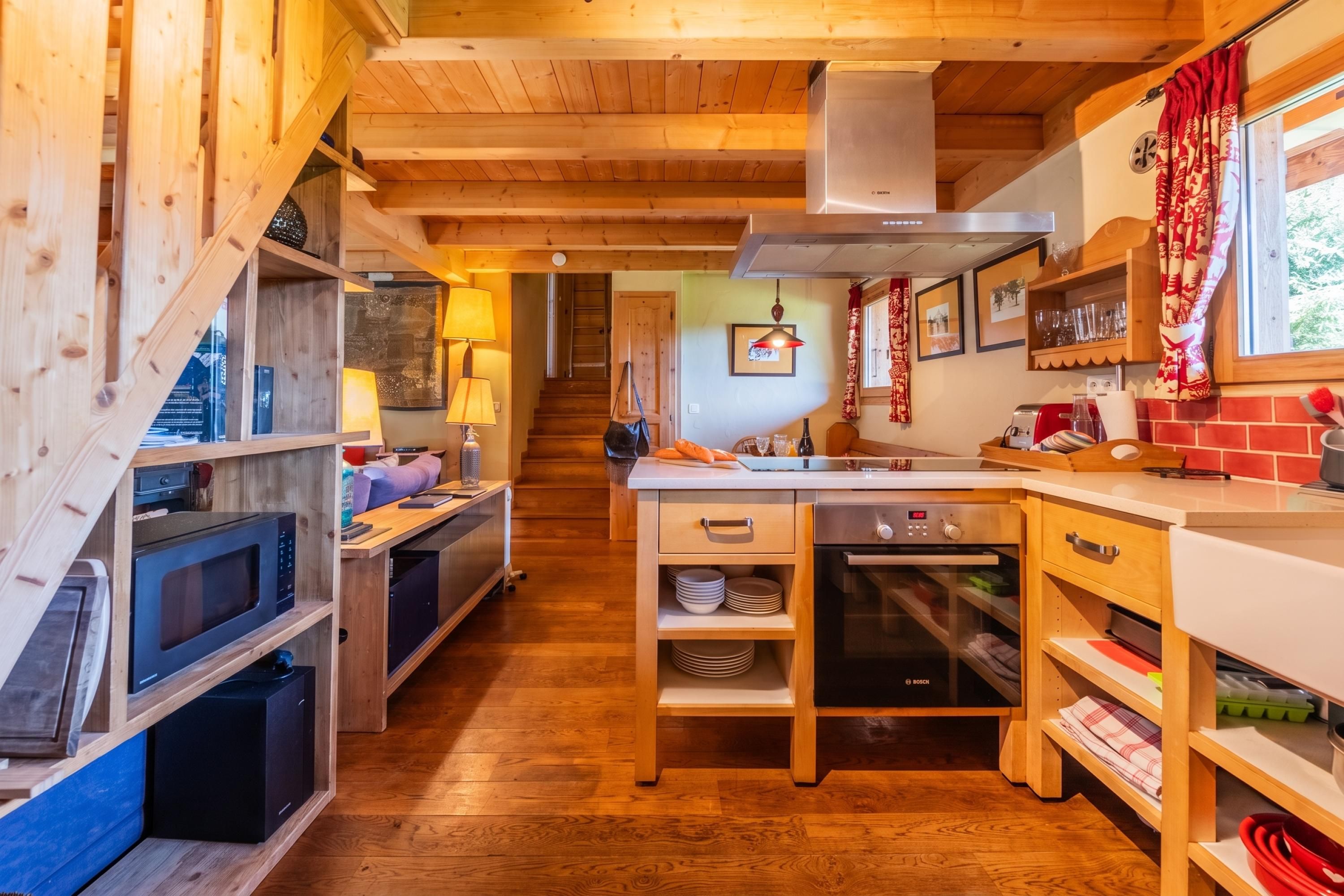 Een kleine keuken met houten kastjes, een Bosch vaatwasser en een raam met rode gordijnen.