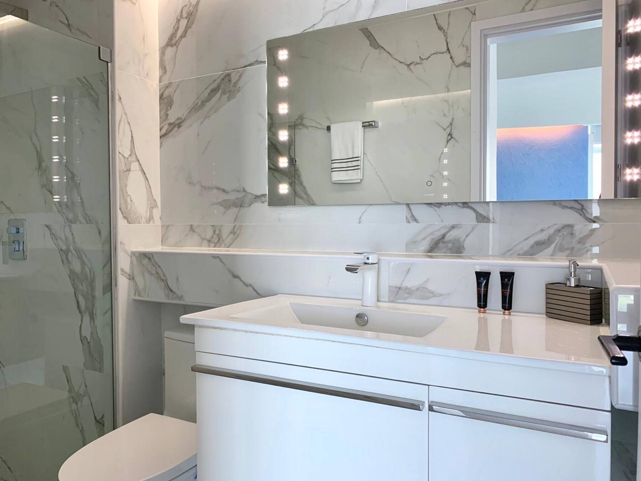 Une salle de bain avec un mur en marbre, un lavabo avec un miroir et un espace douche.