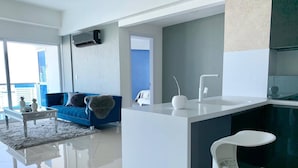 Een moderne woonkamer met een blauwe bank, een witte salontafel en een keuken met een wit aanrecht en een witte stoel.
