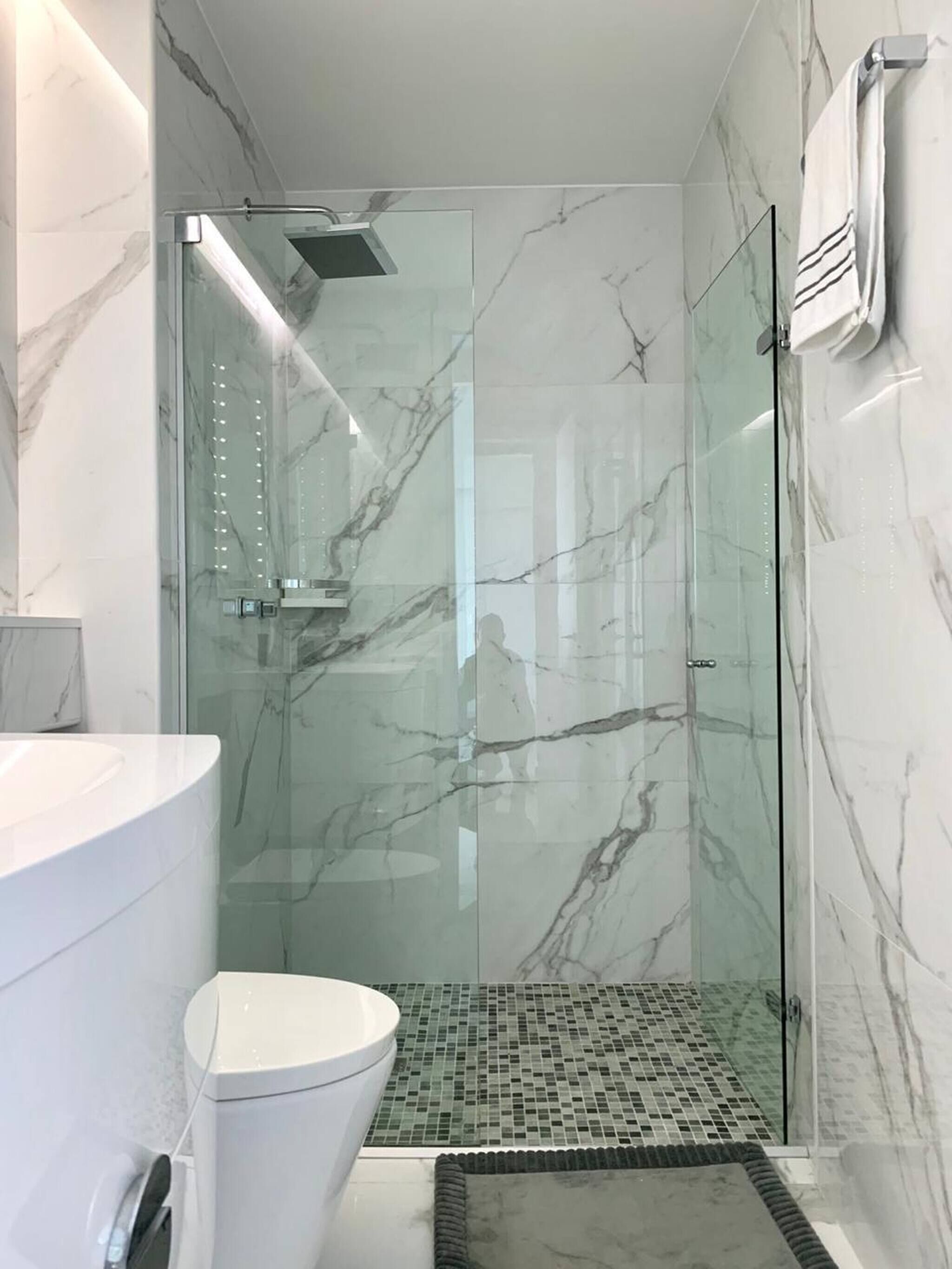 A modern bathroom with a glass shower enclosure, a white toilet, and a marble-tiled floor.