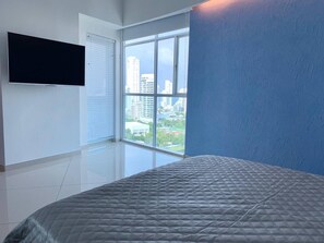 Ein Schlafzimmer mit großem Fenster, einem Bett und einem an der Wand befestigten Flachbildfernseher.