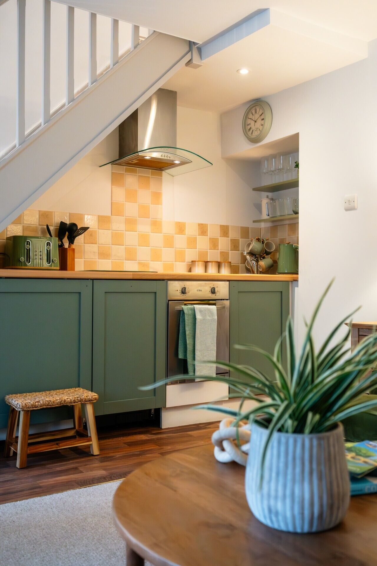 A kitchen with a staircase, a clock, and a plant.