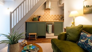 A compact living space with a staircase leading to a kitchen, a green sofa, and a coffee table with books.