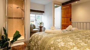 A bedroom with a large bed, a shower, a window, and a wooden door.