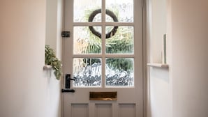 A white door with a wreath, a mailbox, and a small plant on the left.