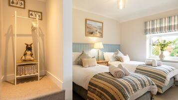 A bedroom with a bed, a nightstand, a lamp, a window with curtains, and a wall-mounted shelf with a stuffed toy.