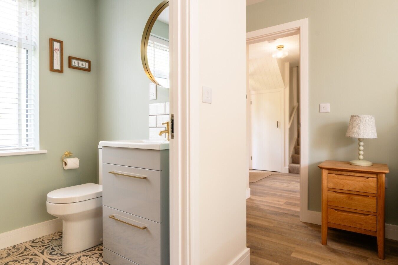 A bathroom with a toilet, a vanity with drawers, a mirror, and a small bedside table with a lamp.