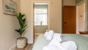 Een slaapkamer met een bed, een bloempot, een houten deur en een raam met zonwering.