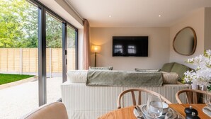Een moderne woonkamer met een bank, een flatscreen televisie en een eethoek met een tafel gedekt voor twee personen.