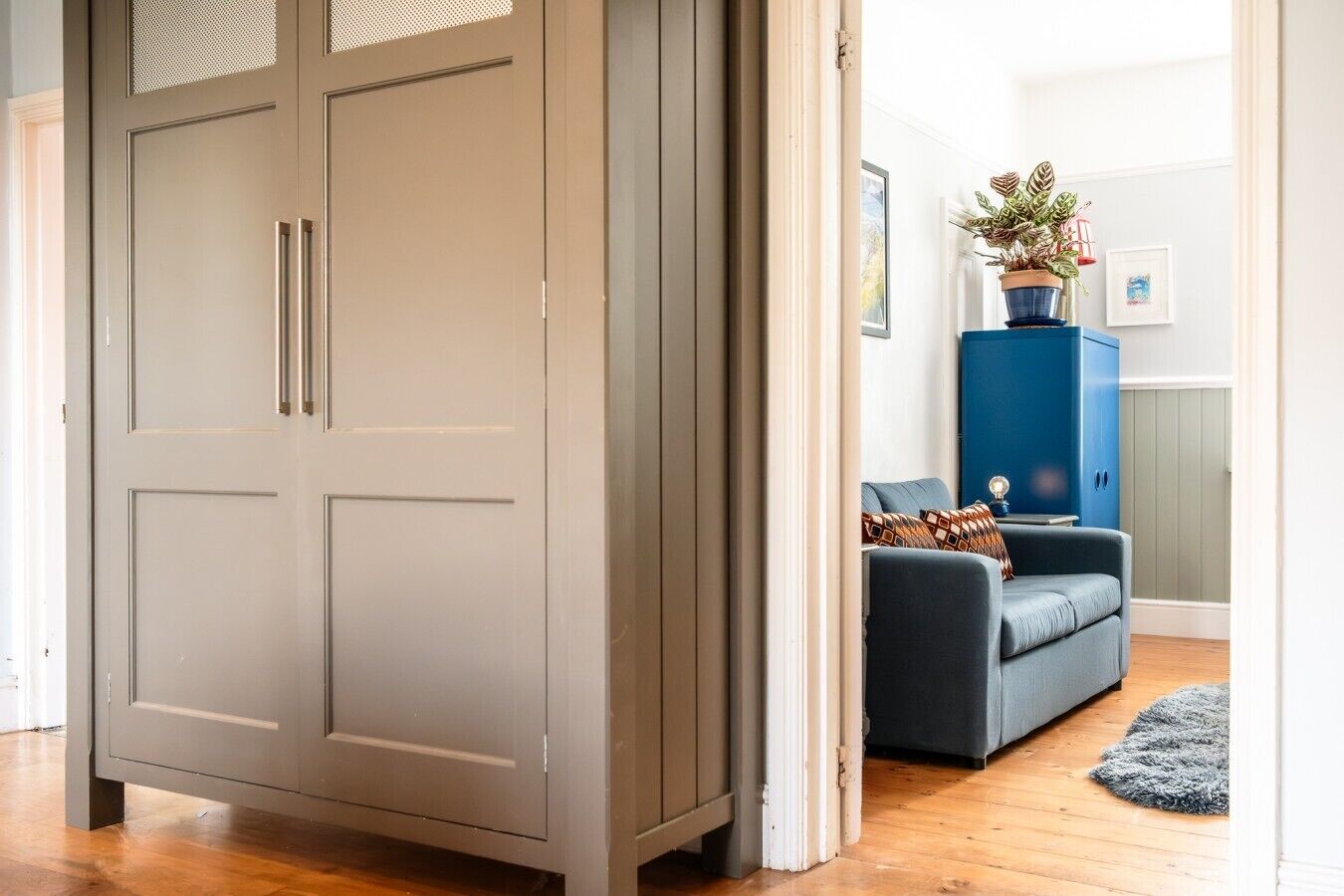 A room with a grey wardrobe, a blue cabinet, a grey sofa, and a small rug.