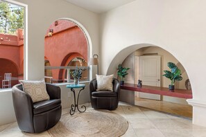 A room with two leather armchairs, a small round table, and a large window with a view of an arched structure outside. - Historic & Modern, Two Hot Tubs, Great For Groups, Central Courtyard (Sedona)