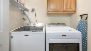 Pesuhuoneessa on kaksi Maytag-merkkiä olevaa pesu- ja kuivauskonetta, niiden yläpuolella puinen kaappi ja pyyheteline, jossa on kuvioitu pyyhe.