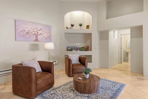 A living room with two brown leather sofas, a round wooden coffee table, a patterned rug, a wall-mounted lamp, and a shelf with books and decorative items. - Historic & Modern, Two Hot Tubs, Great For Groups, Central Courtyard (Sedona)