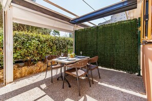 An outdoor patio with a table set for two, surrounded by chairs, a glass enclosure, and a green hedge. - Cabrera Apartment by Mallorca Infinity (Peguera)