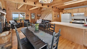 Interior de una cabaña de madera con comedor, cocina y escalera.