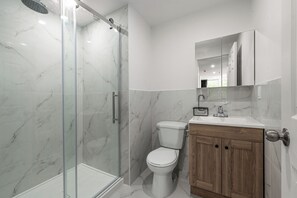 Un baño con ducha de vidrio, inodoro blanco y muebles de madera.