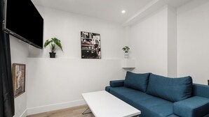 A modern living room with a blue sofa, a white coffee table, and a flat-screen TV mounted on the wall.