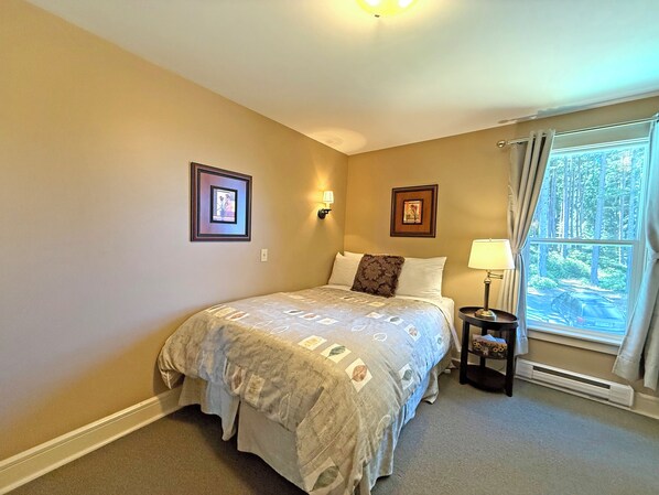 A bedroom with a bed, two wall-mounted lamps, a window with curtains, and two framed pictures on the wall.