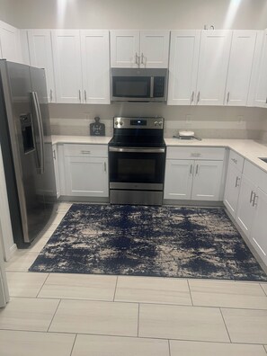 A kitchen with white cabinets, stainless steel appliances, and a blue patterned rug. - 3-bedroom condo in tranquil Wimauma with AC comfort (Wimauma)