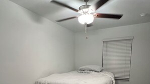 A bedroom with a bed, a ceiling fan, a window with blinds, and a patterned rug.