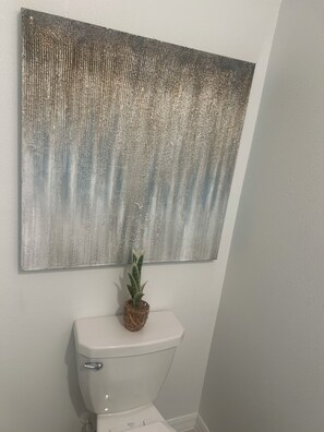Ett badrum med en toalett, en tavla som hänger på väggen och en krukväxt.
