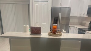 A kitchen with a white countertop, two white bar stools, a refrigerator, and a door with a white frame.