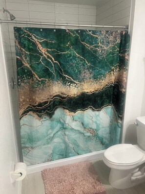 A bathroom with a shower curtain featuring a marble-like pattern, a toilet, and a pink rug. - 3-bedroom condo in tranquil Wimauma with AC comfort (Wimauma)