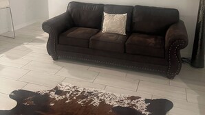 A living room with a brown leather sofa, a cowhide rug, a wall-mounted picture of a bull, a ceiling fan, and a staircase.