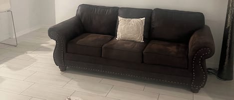 Un salon avec un canapé en cuir marron, un tapis en peau de vache, un tableau représentant un taureau accroché au mur, un ventilateur de plafond et un escalier.