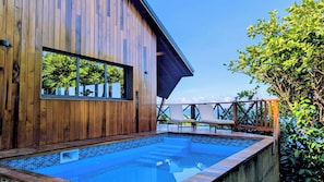 A wooden building with a swimming pool, a lounge chair, and a view of the ocean.