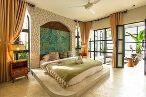 A bedroom with a stone arch, a bed with a green blanket, a nightstand, and a view through large windows. - Romantic Mediterranean Pool Villa (Seminyak)