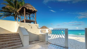 Ein Hotel am Strand mit einem strohgedeckten Bauwerk, einem weißen Tor und einer Treppe, die zum Strand führt.