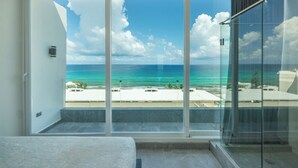 Ein Zimmer mit einer großen Schiebeglasdoor, die auf einen Balkon mit Meer- und Strandblick führt.