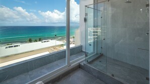 Ein modernes Badezimmer mit Duschkabine aus Glas, einem großen Fenster mit Blick auf Strand und Meer.