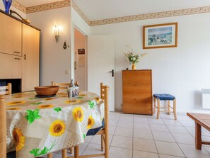 Ein Essbereich mit einem Tisch, der mit einer sonnenblumenmuster Tischdecke bedeckt ist, Holzsesseln, einem Holzschrank und einem gerahmten Bild an der Wand.
