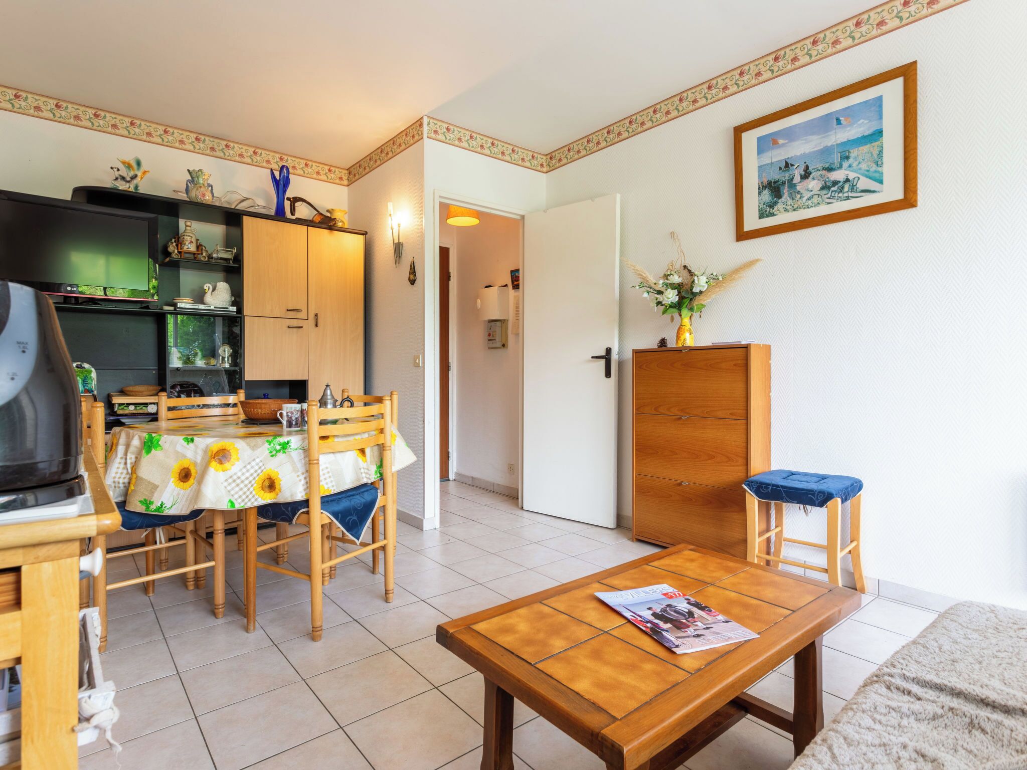 Ein gemütliches Wohnzimmer mit einem Holzesstisch, Stühlen, einem Couchtisch, einem Fernseher und einer Küchenzeile mit Schränken und einem Kühlschrank.
