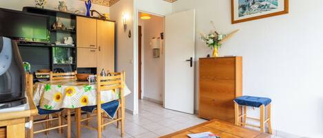 Ein gemütliches Wohnzimmer mit einem Holzesstisch, Stühlen, einem Couchtisch, einem Fernseher und einer Küchenzeile mit Schränken und einem Kühlschrank.