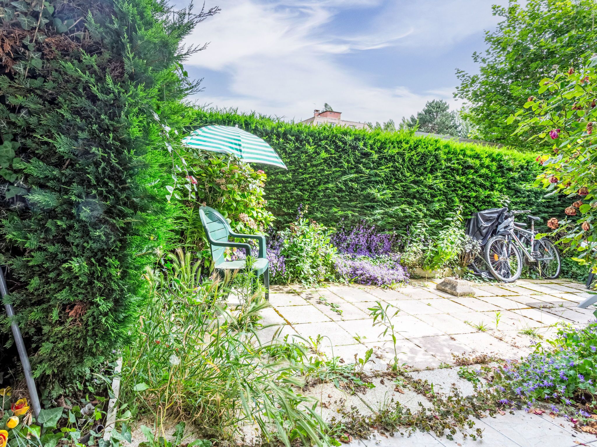 A garden patio with a green chair, a bicycle, and a striped umbrella.
