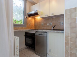 A compact kitchen with a dishwasher, oven, and a window with a view of greenery. - Les Portes de la Mer by Interhome (Villers sur mer)