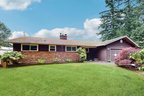 Une maison de plain-pied avec une façade en briques, un toit en pente et un petit jardin à l’avant.
