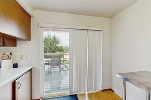 Une cuisine dotée d’un plan de travail blanc, d’un meuble en bois et d’une porte-fenêtre coulissante donnant sur une terrasse extérieure.