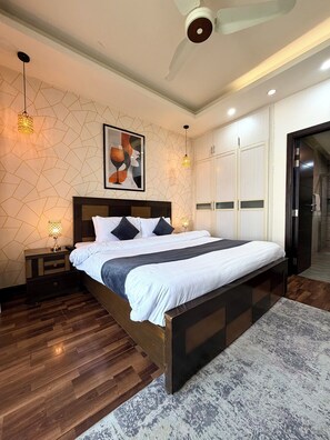 Ein Schlafzimmer mit einem großen Bett, Holzboden, Deckenventilator und einer Wand mit geometrischem Muster.