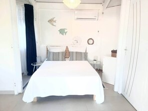 A bedroom with a bed, a bedside table, a small table, and a wardrobe. - Cocoon Cap (Sainte-Anne)
