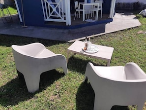 Outdoor seating with a table and chairs, a small table with a glass and bottle, and a blue building in the background. - Cocoon Cap (Sainte-Anne)