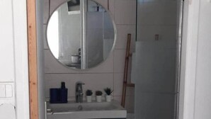 Un baño con espejo redondo, lavabo y mueble.