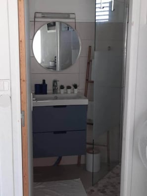 A bathroom with a round mirror, a sink, and a cabinet. - Cocoon Cap (Sainte-Anne)