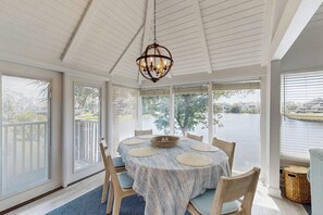 A dining area with a round table, chairs, and a chandelier. - Lakefront house w/screened-in patio, pool, close to beach & golf (Pawleys Island)