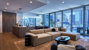 Ein modernes Wohnzimmer mit einer Couch, einem Couchtisch und Blick auf die Stadt durch große Fenster.