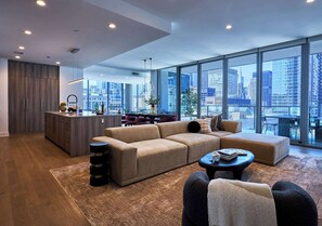 Una sala de estar moderna con un sofá, una mesa de centro y vistas de la ciudad a través de amplios ventanales.