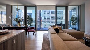 Ein modernes Wohnzimmer mit Sofa, Esstisch und Stühlen, großen Fenstern mit Stadtblick und hängenden Pendelleuchten.